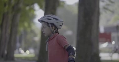 Kask takan ve koruyucu giysiler giyen genç bir çocuğun yakın çekimi. Kolunu dışarı uzatarak bir an için dengesini kaybediyor.