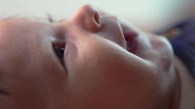 Bir bebeğin yan profilini yakın plan çekerken yere uzanmış, yukarıyı yumuşak bir ifadeyle seyrediyor. Bebek evde huzur içinde dinleniyor, sakin ve meraklı bir bakışla çevreyi gözlemliyor.