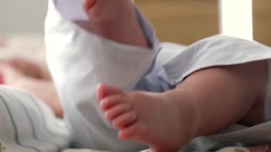 Yatakta yatarken giysiden fırlayan bebek ayağının yakın çekimi. Bebeklerin küçük ayak parmaklarına ve yumuşak cildine odaklanır, ayakların nazik hareketlerini vurgular.
