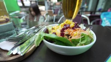 Açık bir restoran masasında mısır ve pancar da dahil olmak üzere çeşitli sebzelerle taze bir salatanın yakın çekimi. Sağlıklı beslenme ve canlı bir yemek atmosferi.