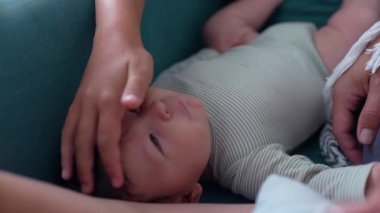 Bebek kanepede yatarken bir el nazikçe başını okşuyor. Sakin, şefkatli bir an bebek ve bakıcı arasındaki yakınlığı ve şefkati yansıtıyor.