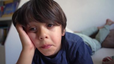 Yatakta başı destekli bir şekilde yatan genç çocuk, düşünceli bir ifadeyle geleceğe bakıyor. Sakin ve düşünceli bir an sessiz ve içsel bir ruh hali olduğunu gösteriyor.