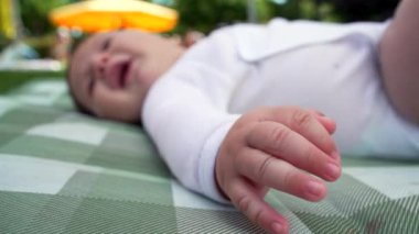 Bebek battaniyeye uzanmış, elini kameraya doğru uzatmış. Açık park ayarı erken gelişim ve keşif gösterileri, bebekliğin doğal merakını yakalıyor