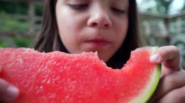 Genç bir kız yüzüne bir dilim karpuz dayayıp bir ısırık daha almaya hazırlanıyor. Odaklanmış ifadesi ve canlı meyvesi canlandırıcı bir yaz sahnesi yaratıyor.