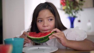 Yemek masasında oturmuş bir dilim karpuz yiyen bir kız. Konforlu bir ev ortamında günlük yemek zamanı