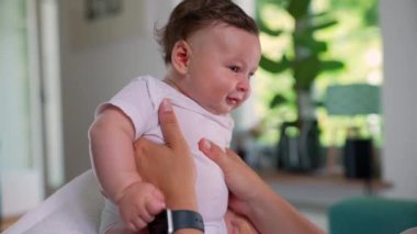 Bebek bir yetişkin tarafından tutuluyor, rahat bir ev ortamında ilginç bir şekilde etrafına bakıyor, keşif ve keşif anını yakalıyor.