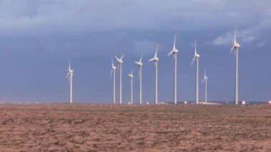 Kurak bir çöl manzarasında rüzgâr türbinleri sıralanır. Temiz enerji teknolojisi rüzgarın gücünden faydalanıyor. Geniş bir arazide bulutlu bir gökyüzüne karşı kurulmuş.