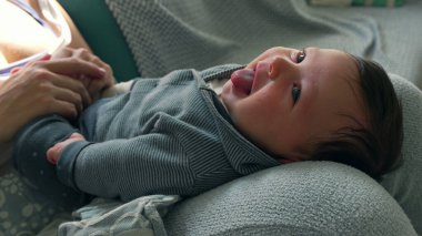 Happy baby lying on a cozy surface, smiling up at the camera. The close-up captures the joyful innocence and playful mood, highlighting the warmth and love in the home clipart