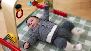 Bebek paspasın üzerinde uzanıyor, merakla renkli oyuncaklara bakıyor. Rahat bir odada eğlenceli bir düzen, bebeğin erken gelişim aşamalarını ve dünyaya olan hayranlığını ön plana çıkarıyor. 