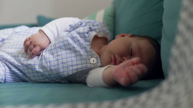 Kanepede uyuyan bir bebeğin, huzurlu ve huzurlu bir anı yakaladığı yakın plan. Samimi ortam ve yumuşak ışıklandırma bebeğin sükunetini ve masumiyetini vurguluyor.