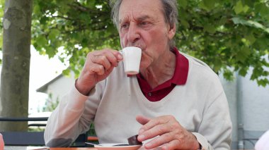 Dışarıdaki yaşlı adam küçük beyaz bir bardaktan espresso yudumluyor, rahatlamanın tadını çıkarıyor.