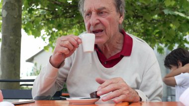 Dışarıdaki yaşlı adam küçük beyaz bir bardaktan espresso yudumluyor, rahatlamanın tadını çıkarıyor.