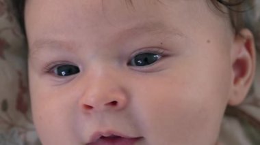 Bebek yüzünün yakın çekimi merak ve yumuşaklık gösteriyor, bebek doğrudan büyük gözlerle bakıyor, bebek hassas özellikleri odak noktasında, sakin ve rahat yüz ifadesi, bebek bakımı nazikçe