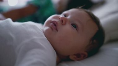 Bebeğin sırtüstü yatışı, meraklı gözlerle yukarı bakışı ve hafif yarık dudaklar, bebeğin barışçıl ifadesini ve narin özelliklerini gösteriyor..
