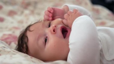 Bebek battaniyesinin üzerinde sakin bir ifadeyle dinleniyor, bebek usulca bakıyor, yüz hatları gevşiyor, bebek huzurlu bir tavırla uzanıyor, huzurlu ve hoşnut bir bebek dinleniyor.