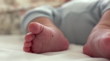 Bir yatakta dinlenen bebek ayaklarının yakın çekimi, rahat ve huzurlu kapalı bir ortamda yumuşak cilt ve küçük ayak parmaklarını yakalamak, erken çocukluğun hassasiyetini gösterir.