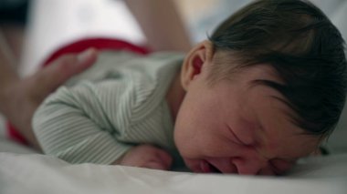 Anne, ağlayan yeni doğmuş bebeğini nazikçe yataktan kaldırıyor. Rahatlatıcı bir dokunuşla sıkıntılı bebeği sakinleştiriyor. Bakım bakımını vurguluyor ve hassas bir anda bağ kuruyor.