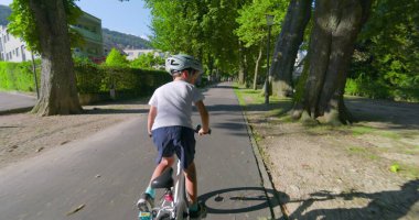 Genç bir çocuk şehir ortamında bisiklet sürüyor, koruma için kask takıyor, güneş parıldıyor, açık hava aktiviteleri sergiliyor.