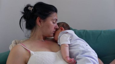 Anne ve bebek kanepede sessiz ve samimi bir anı paylaşırlar. Sarılmaları, huzurlu bir yuvada derin bir bağ ve sıcaklığı yansıtır.