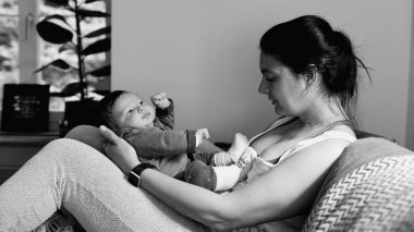Anne kanepeye oturmuş, bebeğini kucağında tutuyor ve onlara sevgiyle bakıyor. derin bağ ve bağlantı, tek renkli siyah beyaz