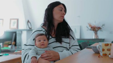 Anne, gülümseyen bebeğini oturma odasında nazikçe tutuyor. Sıcak ve samimi ortam anne ve çocuk arasındaki sevgi ve neşe dolu bağı vurguluyor.