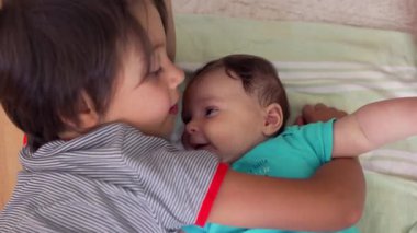 Küçük çocuk, küçük kardeşine şefkatle sarılıyor, sevgi dolu ve neşeli bir aile anını yakalıyor.