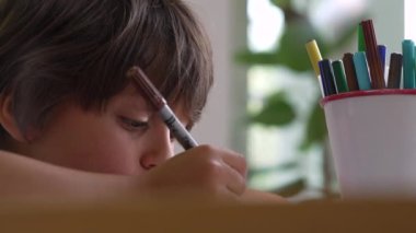 Çizime çok dalmış genç bir çocuğun yan profili. Üzerinde yoğunluk olan kahverengi bir işaret var. Yan tarafında renkli işaretler var.