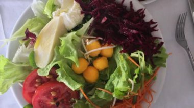 Beyaz bir tabakta servis edilen renkli taze sebze salatası, marul, domates, doğranmış pancar, kavun topları ve peynir, sağlıklı ve canlı bir yemek için düzenlenmiştir.