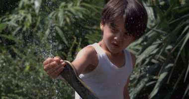 Child smiling and playing with water splashes in slow motion at 800 fps, enjoying the outdoor fun on a sunny day clipart