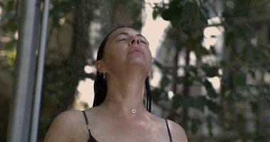 Soğuk su deresinin altında duran bir kadının ağır çekimde, başı arkaya eğilmiş, gözleri kapalı, ve su damlacıkları yüzünde parıldıyor, yemyeşil, yemyeşil bir ortamda.