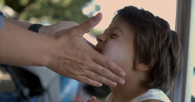 Bir çocuğun yüzüne 800 fps 'de yavaş çekimde güneş kremi sürmek, açık hava aktiviteleri sırasında hassas cilde verilen koruma ve bakımı vurgulamak