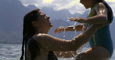 Mother lifts daughter from water in slow-motion at 800 fps, capturing a moment of joy and connection against a backdrop of mountains and serene waters clipart