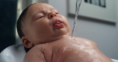 Banyo sırasında bebeğin göğsüne su dökülüyor, bebek yukarı bakıyor ve sakince gülümsüyor, hassas banyo zamanı vücut yıkamaya odaklanıyor. 800 fps yavaş çekim