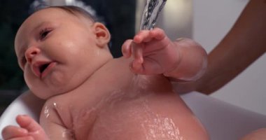 Banyo sırasında bebeğin göğsüne su dökülüyor, bebek başını eğiyor ve sakin görünüyor, rahatlatıcı banyo zamanı vücut bakımı ve hijyene odaklanıyor. 800 fps yavaş çekim