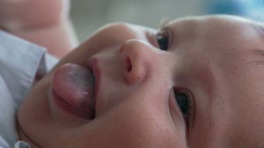 Ağzı açık ve neşeli bir ifadeyle bir bebeğin yüzüne yakın çekim. Bebek yatağa uzanıyor, yukarıya bakıyor, narin özelliklerindeki masumiyet ve mutluluğu vurguluyor.