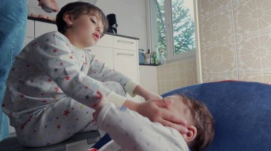 Pijamalı bir çocuk, rahat bir mutfakta küçük bir kardeşle şakalaşıyor. Sıcak, kapalı bir ortamda sevgi ve ilgi dolu bir kardeş anı.