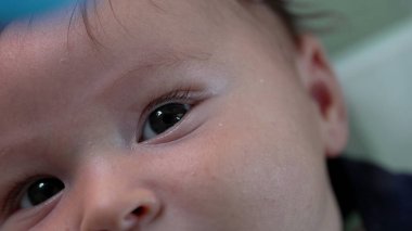 Bebek gözünün ve yüzünün aşırı yakın çekimi, merakla yukarıya bakıyor. Yeni doğmuş bir bebeğin çevreyi gözlerken detaylı görüntüsü.