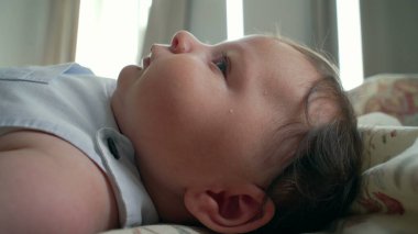 Yatakta uzanan bebek, yandan gören, yumuşak saçlı ve hafifçe gülümseyen.