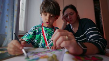 Anne ve oğlu yaratıcı bir çizim faaliyeti içinde, ikisi de birlikte renklendirmeye odaklanmış, huzurlu bir ev ortamında bağ kurma anının tadını çıkarıyorlar.