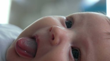 Ağzı açık ve neşeli bir ifadeyle bir bebeğin yüzüne yakın çekim. Bebek yatağa uzanıyor, yukarıya bakıyor, narin özelliklerindeki masumiyet ve mutluluğu vurguluyor.