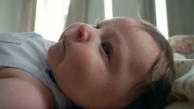 Yatakta uzanan bebek, yandan gören, yumuşak saçlı ve hafifçe gülümseyen.