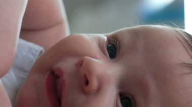 Ağzı açık ve neşeli bir ifadeyle bir bebeğin yüzüne yakın çekim. Bebek yatağa uzanıyor, yukarıya bakıyor, narin özelliklerindeki masumiyet ve mutluluğu vurguluyor.