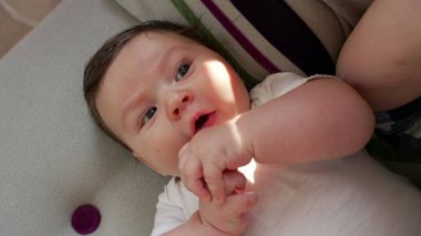 Bebek kanepede uzanıyor, neşeli bir gülümsemeyle ellerini oynatıyor. Erken gelişim ve kendini keşfetme anı konforlu ve besleyici bir ev ortamında