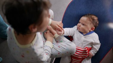 Çocuk bir taburede oturuyor, mutfakta küçük bir kardeşle izliyor ve etkileşim kuruyor. Huzurlu bir aile ortamında kardeş kaynaşması ve sevgi anı.