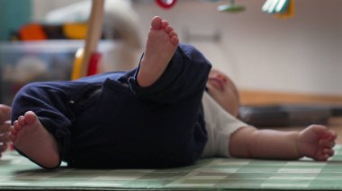 Bir bebeğin oyun hasırının üzerine uzanmış, rahat bir ev ortamında oyun saatinde bebeğin bacaklarını ve ayaklarını rahat bir pozisyonda gösteriyor.