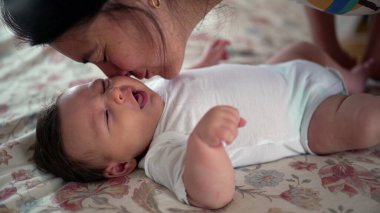 Anne-baba sevgi dolu bir şekilde yatakta uzanmış bebeği öpüyor, şefkat ve sıcaklık gösteriyor, bebeğin geniş gözleri, şefkat ve yakınlık dolu bir ev ortamında baktığı anlar