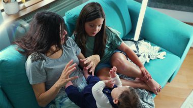 Anne ve kızı kanepede oturuyor, rahat bir aile anında bir bebekle bağ kuruyor ve onunla etkileşime geçiyor, evde bakım ve şefkate odaklanıyor.