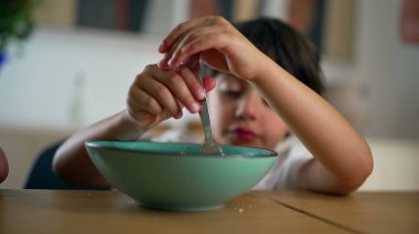 Konsantrasyonlu bir kasede yemek karıştıran genç bir çocuk, evde sakin bir yemek sırasında etkinliğe odaklanmış bir aile ortamında