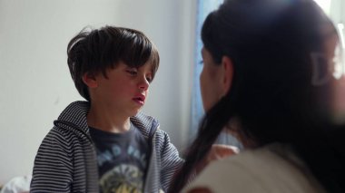 Çocuk ağladıktan sonra gözyaşlarıyla yansıyor, başı hafifçe eğik ve duygularını gösteriyor, kapalı alanda annesiyle olan duygularını işlerken sakin bir an.