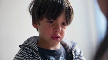 Çocuk ağladıktan sonra gözyaşlarıyla yansıyor, başı hafifçe eğik ve duygularını gösteriyor.